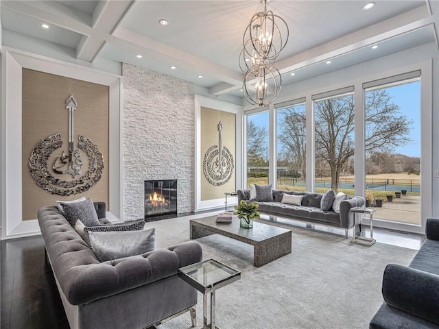 living area with coffered ceiling, beam ceiling, a stone fireplace, a notable chandelier, and recessed lighting