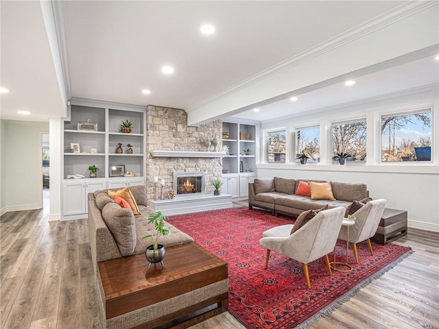 living area featuring light wood-style floors, baseboards, crown molding, and a stone fireplace