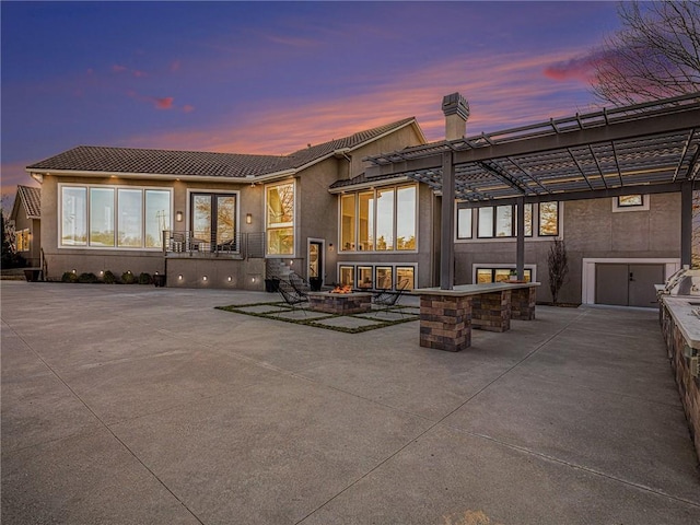 back of house at dusk with stucco siding, a fire pit, a patio, and area for grilling