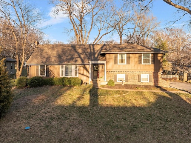 split level home featuring a front yard, fence, brick siding, a chimney, and board and batten siding