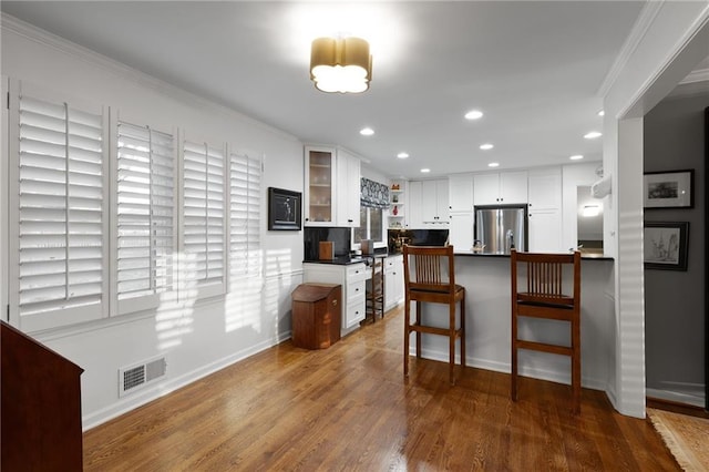 kitchen with visible vents, wood finished floors, white cabinetry, freestanding refrigerator, and glass insert cabinets