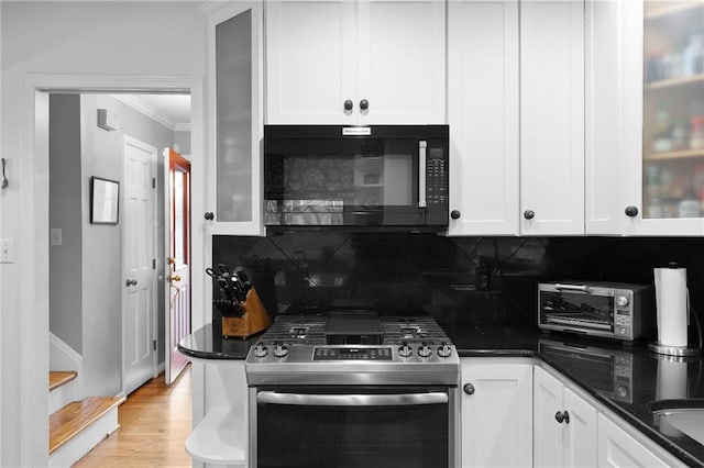 kitchen with stainless steel gas range oven, decorative backsplash, ornamental molding, and white cabinetry