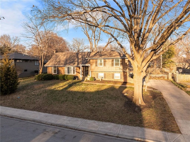 split level home featuring fence, driveway, brick siding, a front lawn, and board and batten siding