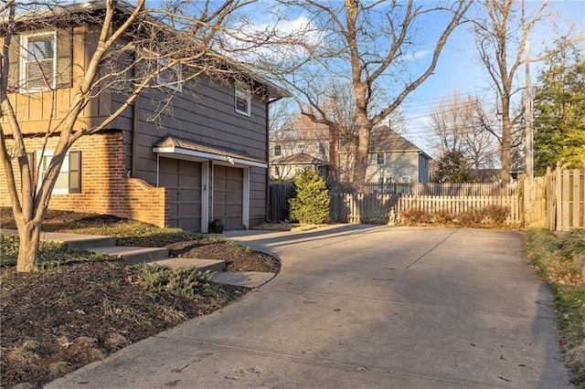 view of side of property featuring brick siding, driveway, an attached garage, and fence