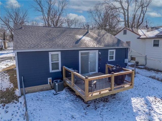 snow covered property featuring a wooden deck, cooling unit, and roof with shingles