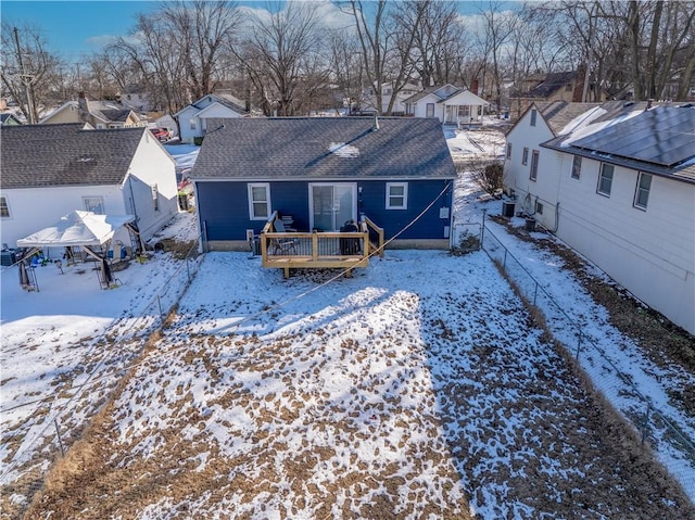 snow covered rear of property with a residential view, roof with shingles, and a wooden deck