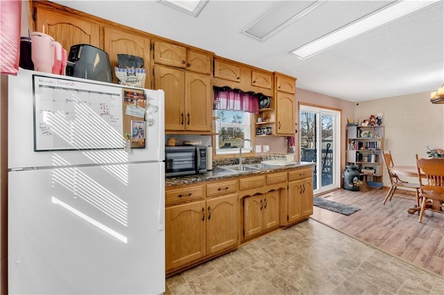 kitchen with dark countertops, stainless steel microwave, brown cabinetry, freestanding refrigerator, and a sink