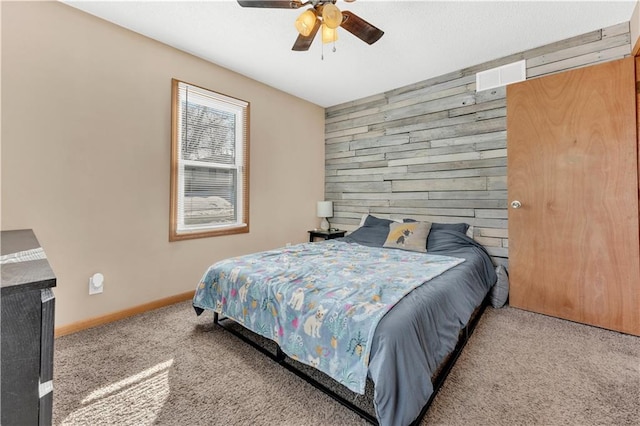 bedroom featuring wooden walls, baseboards, ceiling fan, an accent wall, and carpet