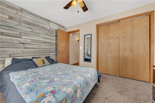 bedroom with carpet floors, wood walls, a closet, and a ceiling fan