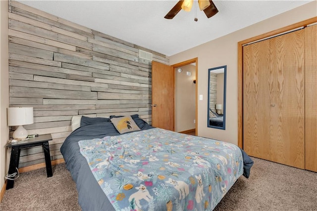 carpeted bedroom featuring wood walls, a ceiling fan, and a closet