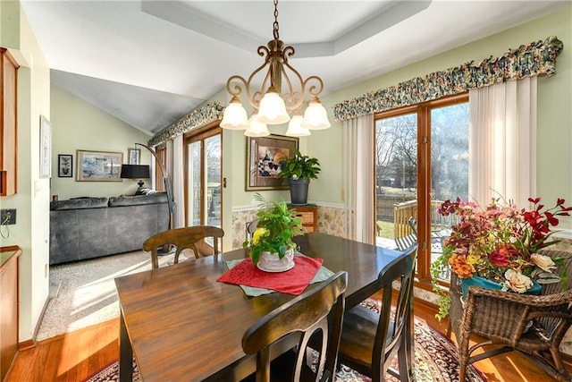 dining room featuring an inviting chandelier, vaulted ceiling, wood finished floors, and a raised ceiling