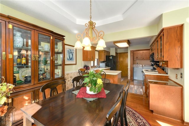 dining space with a raised ceiling, washer and clothes dryer, and wood finished floors