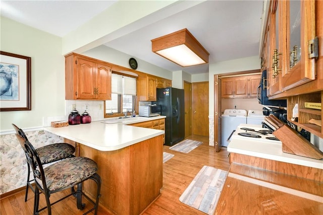 kitchen featuring stainless steel microwave, a peninsula, light wood-style floors, washing machine and dryer, and black fridge