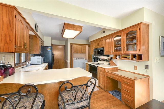 kitchen with brown cabinetry, washing machine and dryer, a sink, a peninsula, and black appliances