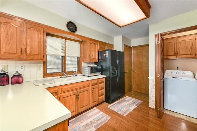 kitchen with a sink, black fridge with ice dispenser, light countertops, backsplash, and light wood finished floors