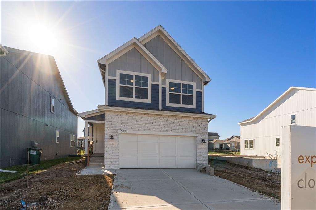 view of front of home with driveway, stone siding, board and batten siding, and an attached garage