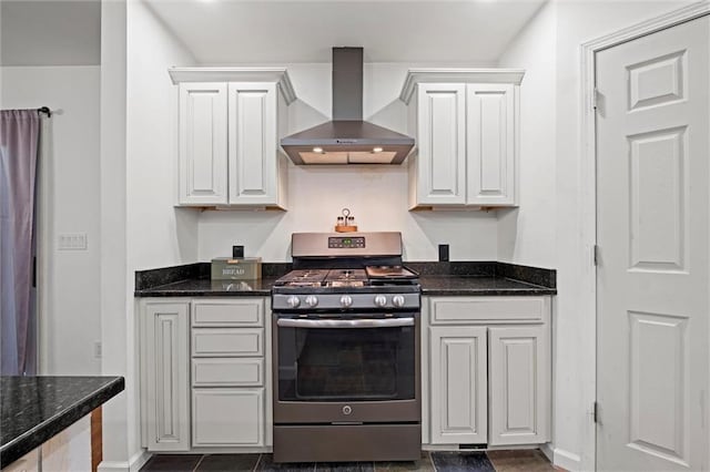 kitchen with dark stone counters, stainless steel range with gas cooktop, white cabinets, and wall chimney exhaust hood