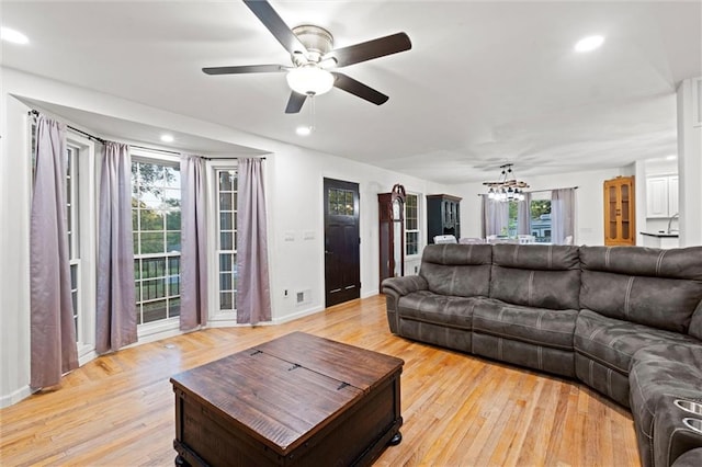 living area featuring light wood-type flooring, recessed lighting, and ceiling fan with notable chandelier