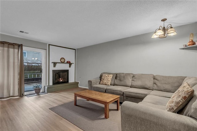 living area featuring a textured ceiling, a chandelier, a large fireplace, wood finished floors, and visible vents