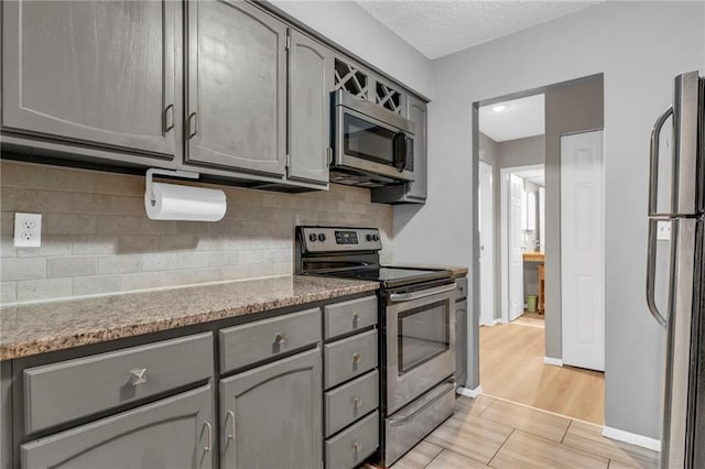 kitchen featuring a textured ceiling, light wood-style flooring, appliances with stainless steel finishes, gray cabinets, and tasteful backsplash