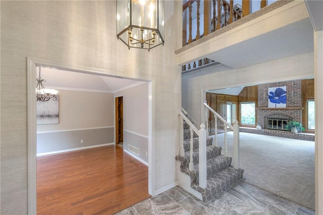 stairs with crown molding, a notable chandelier, a fireplace, baseboards, and visible vents
