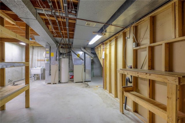 unfinished below grade area with visible vents, a sink, heating unit, and gas water heater