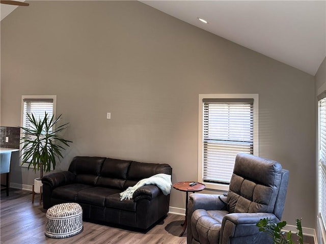 living room featuring high vaulted ceiling, baseboards, and light wood-style floors