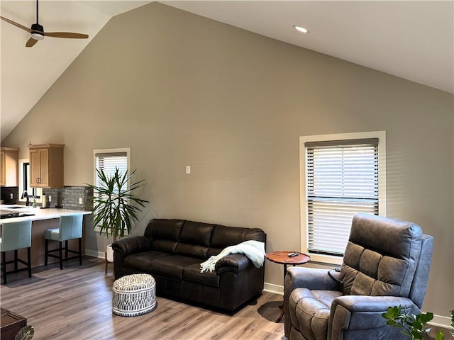 living room with baseboards, high vaulted ceiling, a ceiling fan, and light wood finished floors