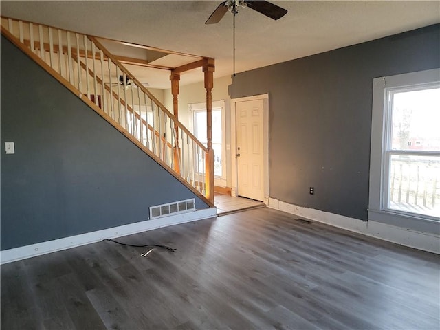 unfurnished living room featuring visible vents, plenty of natural light, stairway, and wood finished floors