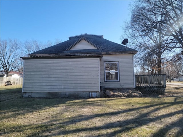 view of side of home featuring a shingled roof, fence, and a lawn