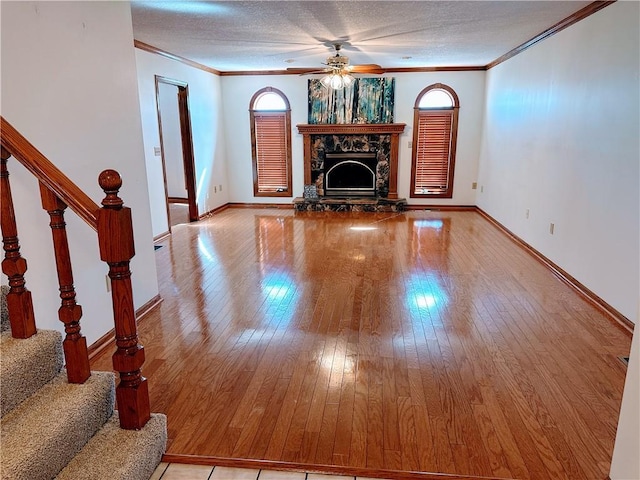 unfurnished living room featuring crown molding, a stone fireplace, a textured ceiling, and light wood-style floors