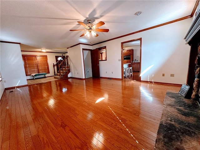 unfurnished living room featuring ceiling fan, hardwood / wood-style flooring, baseboards, ornamental molding, and stairway