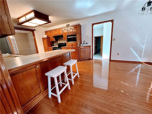 kitchen with electric range, brown cabinetry, a peninsula, light wood-type flooring, and under cabinet range hood