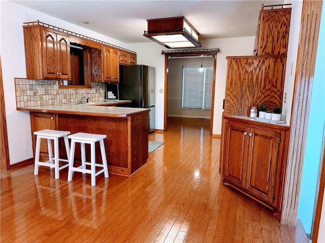 kitchen with a breakfast bar, brown cabinets, light wood finished floors, backsplash, and freestanding refrigerator