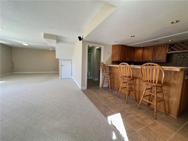 interior space with a kitchen bar, brown cabinetry, light carpet, a textured ceiling, and baseboards