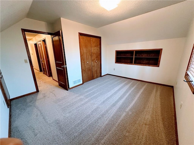 unfurnished bedroom with baseboards, visible vents, vaulted ceiling, a textured ceiling, and a closet