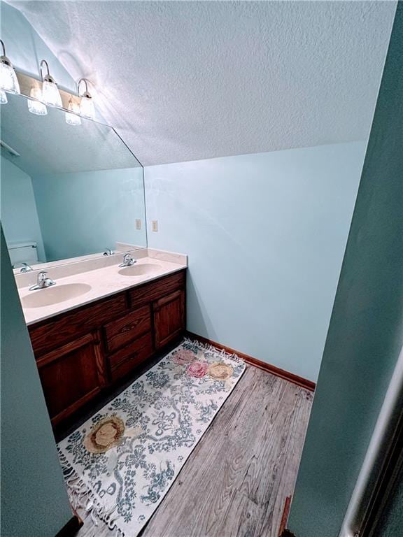 bathroom featuring lofted ceiling, a textured ceiling, a sink, and wood finished floors