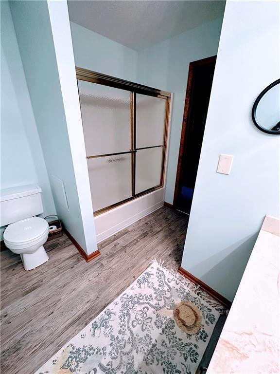 full bathroom featuring wood finished floors, an enclosed shower, toilet, and baseboards