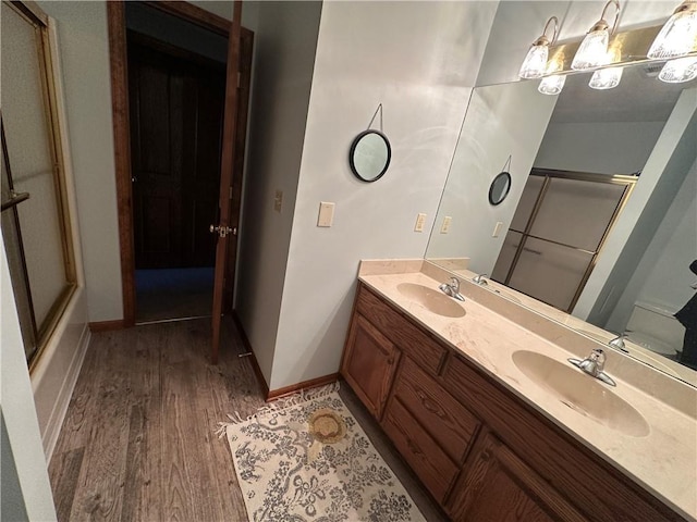 bathroom with double vanity, wood finished floors, a sink, and a shower with shower door