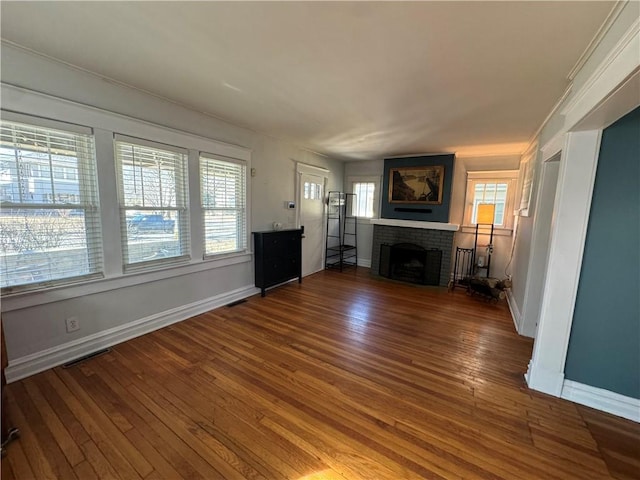 unfurnished living room with a brick fireplace, visible vents, wood-type flooring, and baseboards