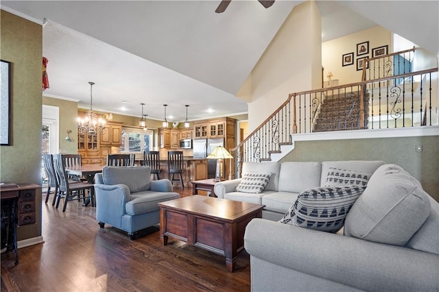 living area featuring dark wood-style flooring, stairs, crown molding, high vaulted ceiling, and ceiling fan with notable chandelier