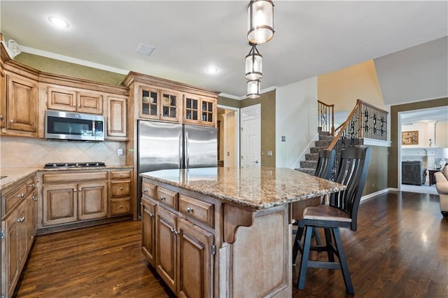 kitchen featuring light stone counters, stainless steel appliances, a kitchen island, dark wood finished floors, and a kitchen bar