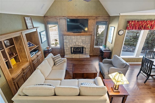 living room with a ceiling fan, lofted ceiling, wood finished floors, crown molding, and a stone fireplace