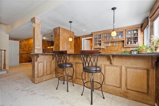 kitchen featuring glass insert cabinets, decorative columns, a kitchen breakfast bar, brown cabinetry, and decorative light fixtures