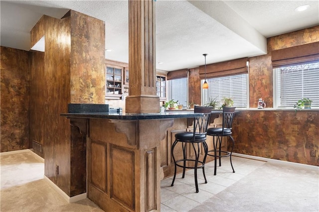 bar featuring decorative columns, light colored carpet, hanging light fixtures, a textured ceiling, and baseboards