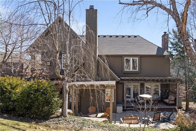 rear view of property with a shingled roof, a patio, and a chimney