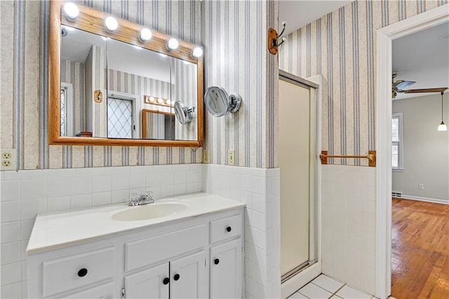 bathroom featuring a shower stall, wallpapered walls, wainscoting, vanity, and a ceiling fan