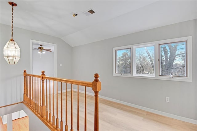 hall with visible vents, baseboards, light wood-type flooring, vaulted ceiling, and an upstairs landing