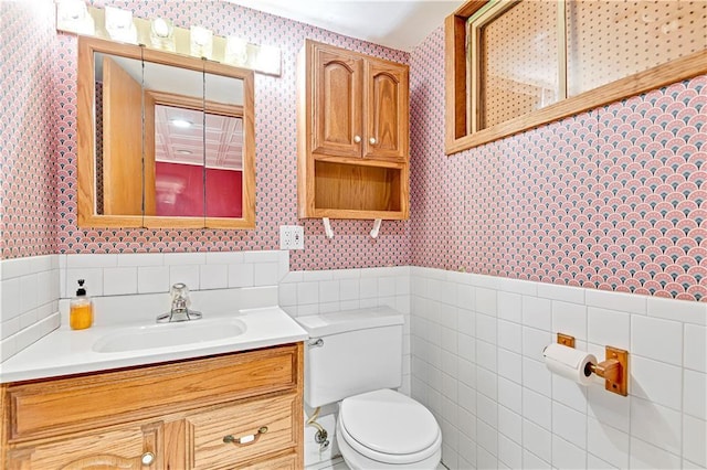 bathroom featuring wallpapered walls, tile walls, toilet, and a wainscoted wall