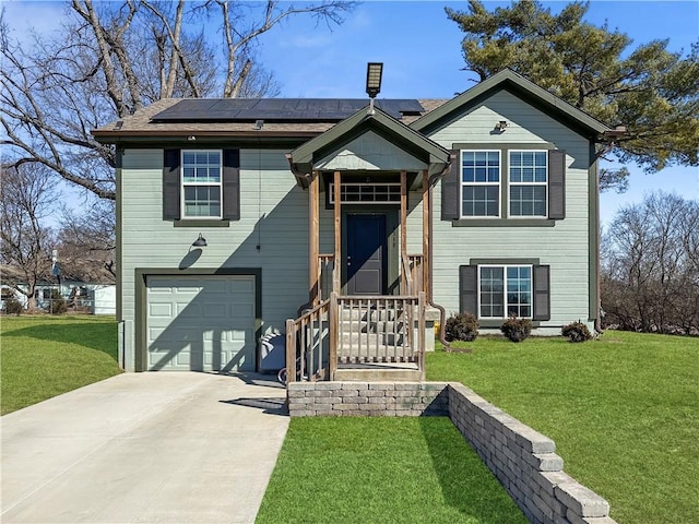 raised ranch featuring a garage, driveway, a front lawn, and roof mounted solar panels